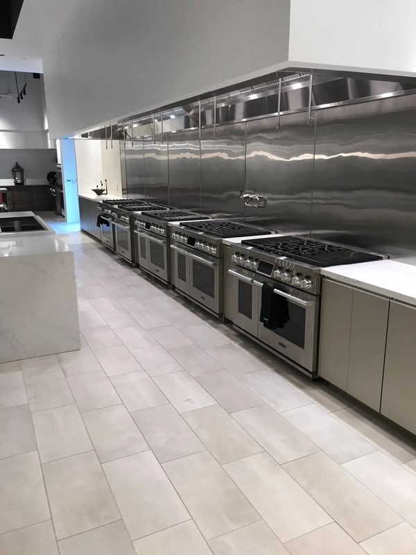 Row of modern stainless steel stoves in a sleek showroom kitchen.