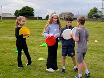 Four children holding colorful frisbees on a grassy field.