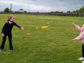 Two girls playing with a yellow frisbee outdoors.