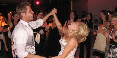 Bride and groom dancing joyfully surrounded by guests.