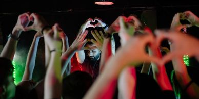 DJ in red shirt surrounded by crowd making heart hands.
