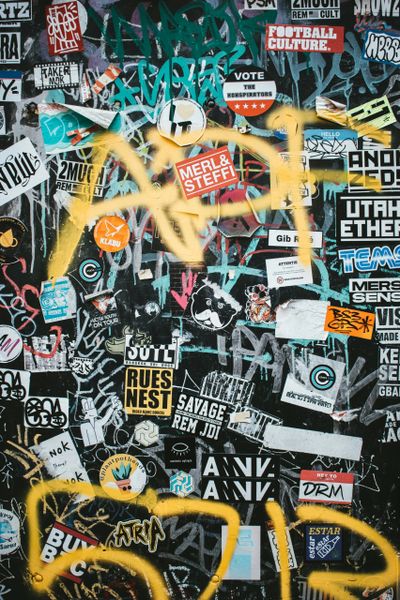 Wall covered with colorful graffiti and layered stickers.