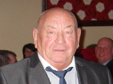 Elderly man in a suit and tie at an indoor event.