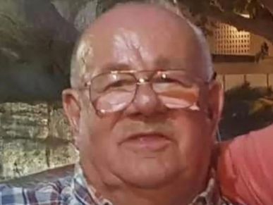 Elderly man wearing glasses and a plaid shirt, smiling gently.