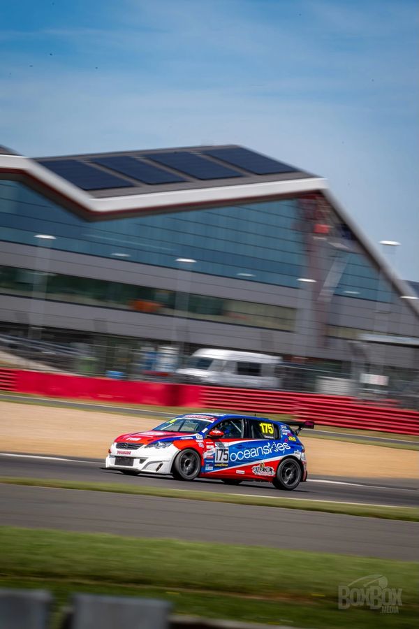 Race car number 175 speeding on a track near a modern building.
