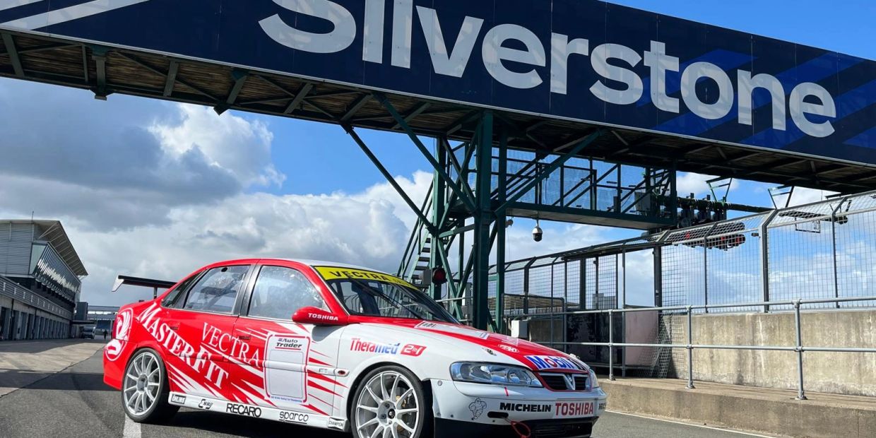 A red and white race car under Silverstone bridge on a sunny day.