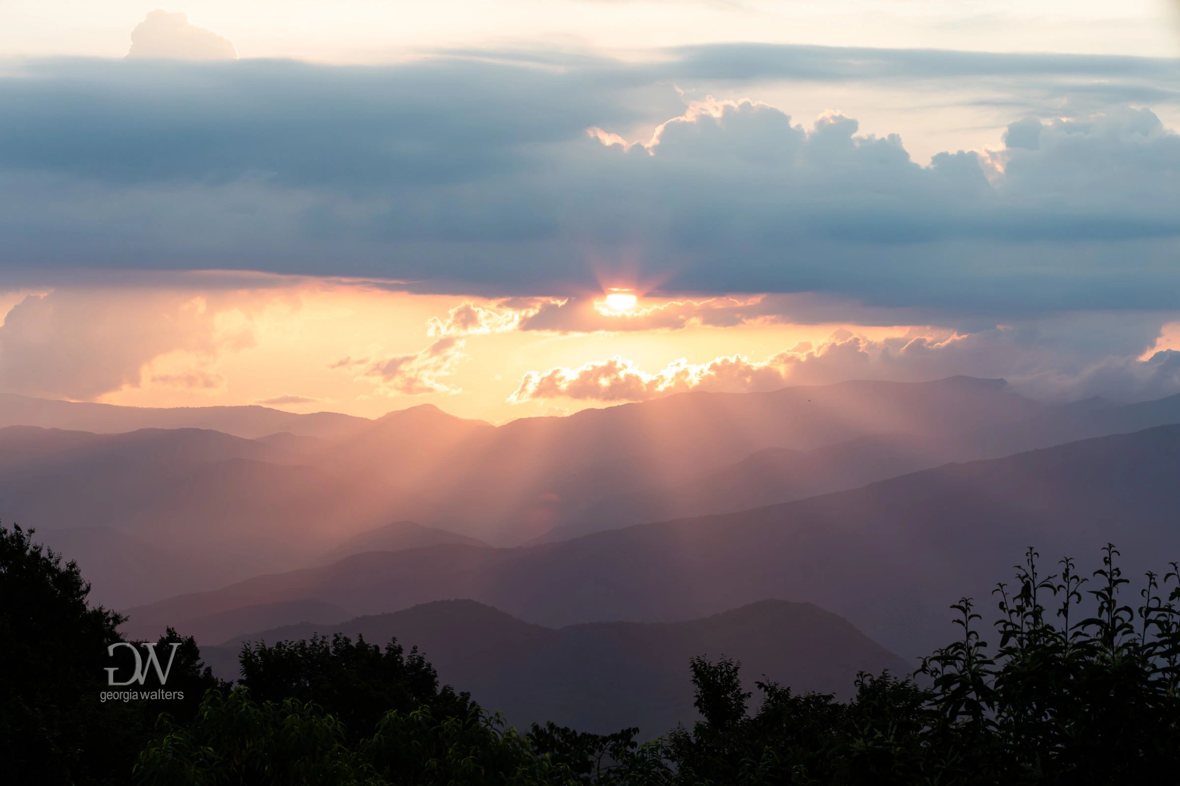 Streaks of sunlight flood over mountain ridges as the sun sets.