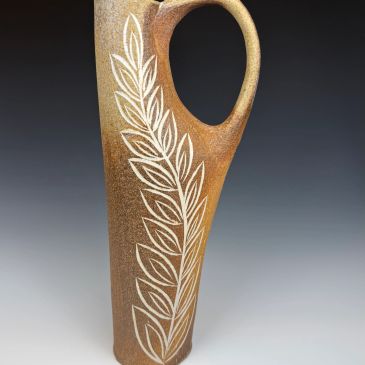 Tall ceramic vase with an engraved leaf design and a curved handle.