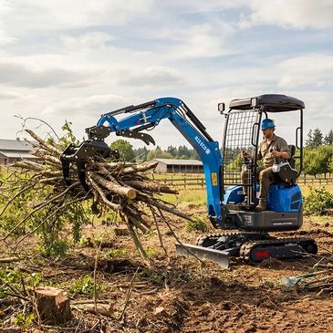 People using a blue mini excavator for yard work and clearing debris.