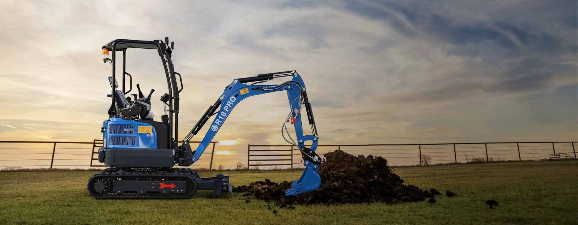 A blue mini excavator digging soil on a grassy field at sunset.