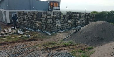Construction of a building with stone walls in progress beside a pile of sand.