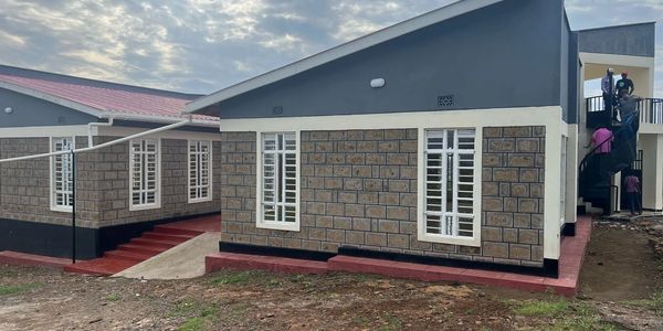 Modern stone-faced building with white windows and a red roof under a cloudy sky.