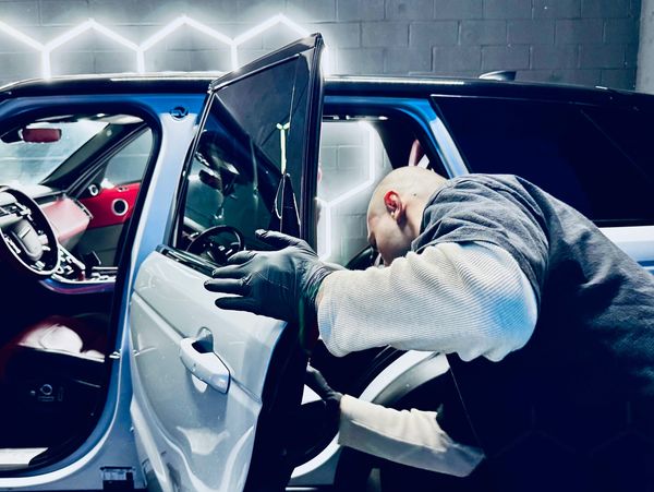 Man wearing gloves inspecting the inside of a car door in a modern garage.