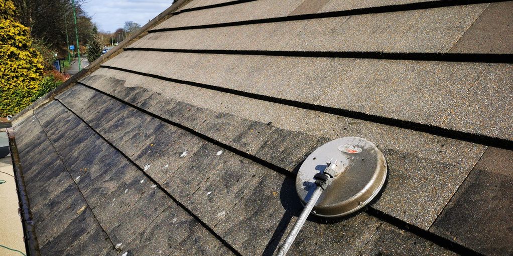 Roof being cleaned with swirly scrubbing tool under blue sky.