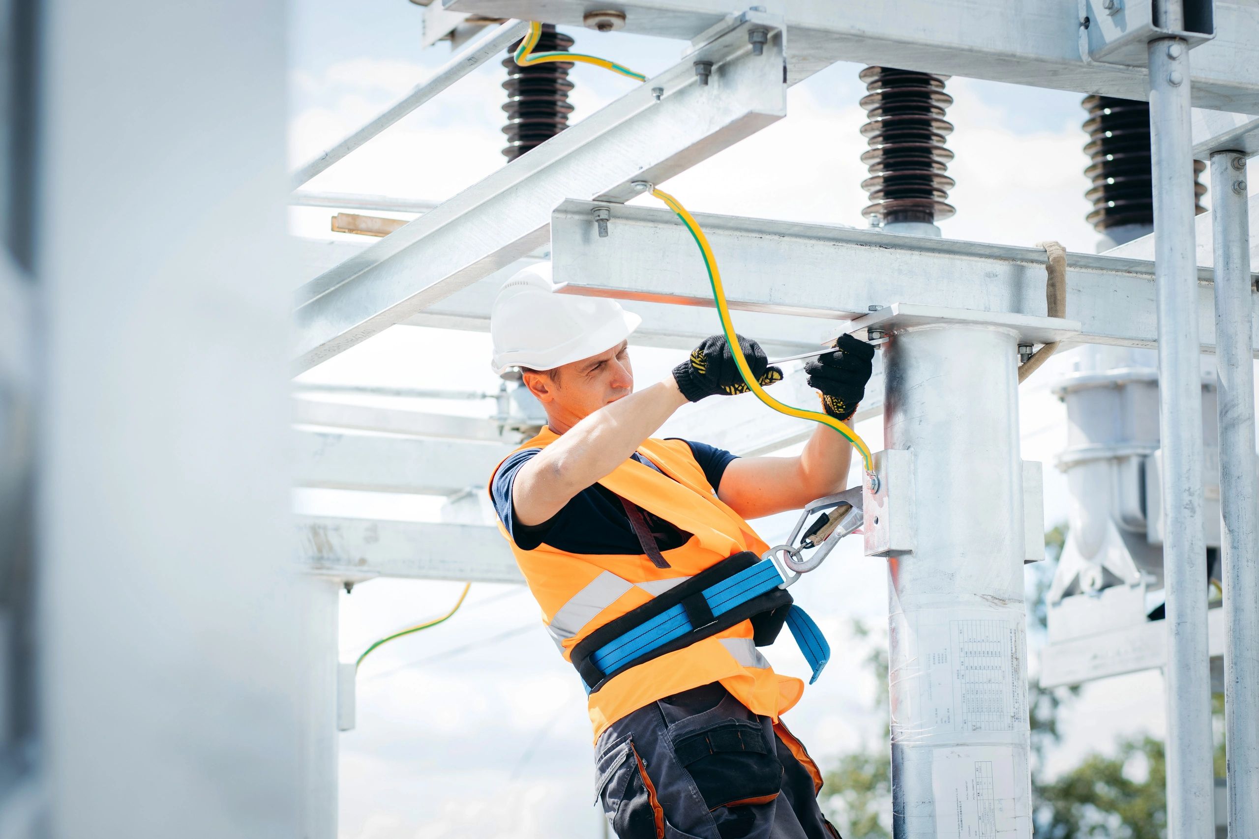 Electrician working on power lines with safety gear and tools.