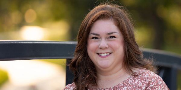 Smiling woman with brown hair outdoors on a sunny day.