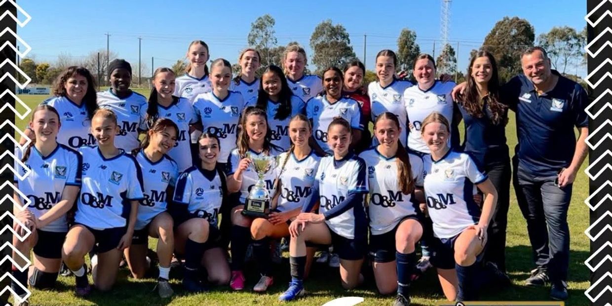A girls' soccer team posing with a trophy on the field.