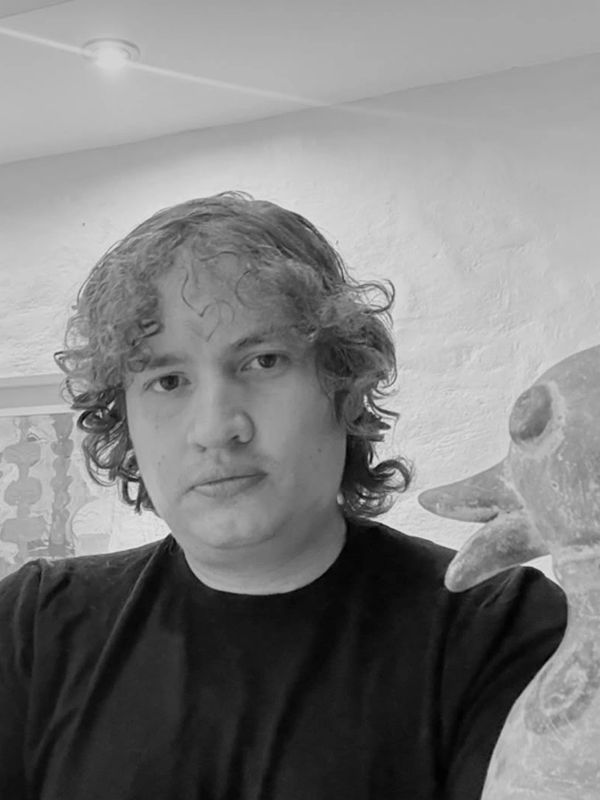 Man with curly hair poses beside a bird sculpture indoors.