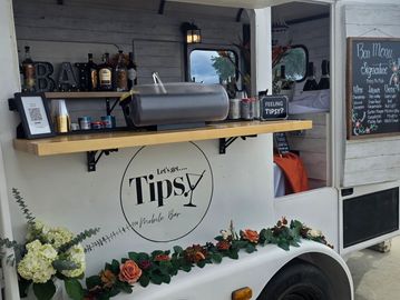 A stylish mobile bar named Tipsy with floral decorations and a drink menu.