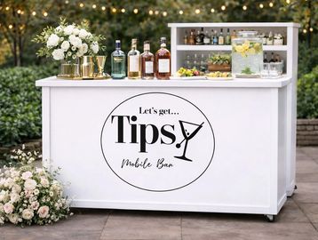 Mobile bar setup with bottles, flowers, and a sign saying 'Let's get Tipsy'.