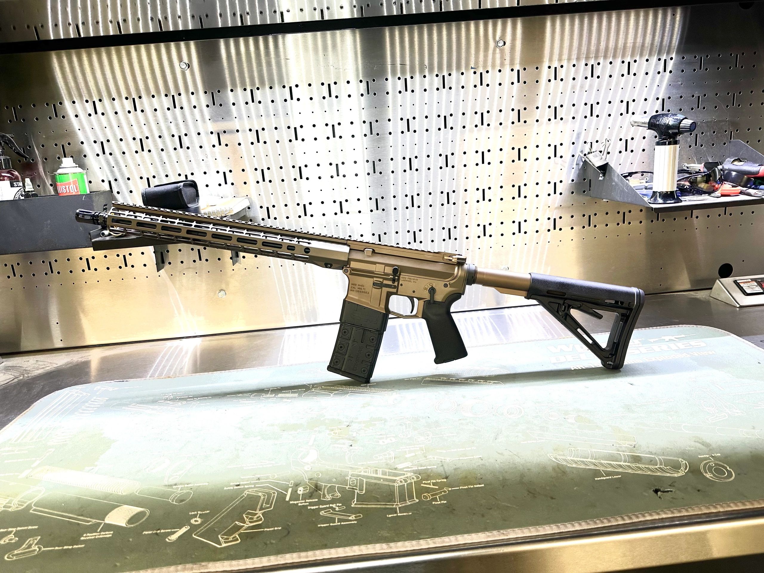 A modern rifle displayed on a workstation mat with weapon diagrams.
