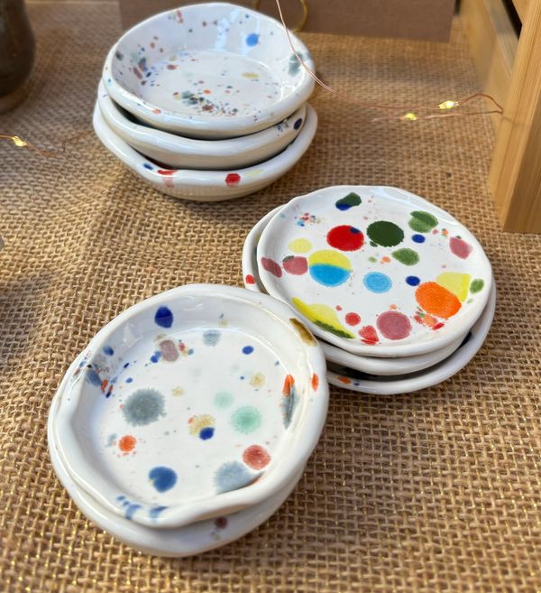 Small ceramic dishes stacked on a brown cloth. They are white with colorful splatters.