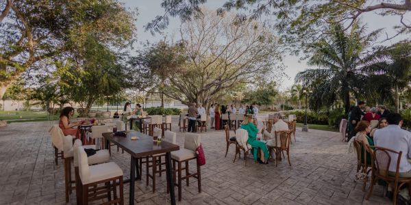 Jardín al aire libre con gente socializando y mesas.