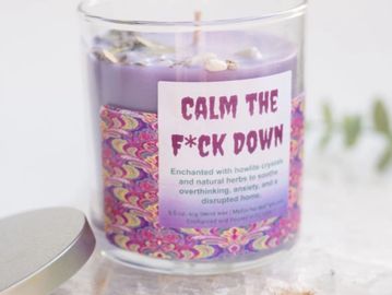 a glass vessel with lavender wax and a colorful label that says calm the f*ck down. silver lid.