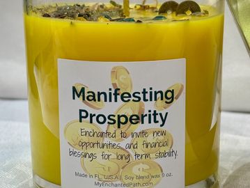 A clear glass jar filled with yellow wax. A label says Manifesting Prosperity, dressed with herbs.