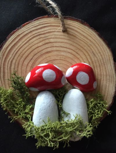 Handcrafted mushrooms with red caps and white spots on a wooden slice.