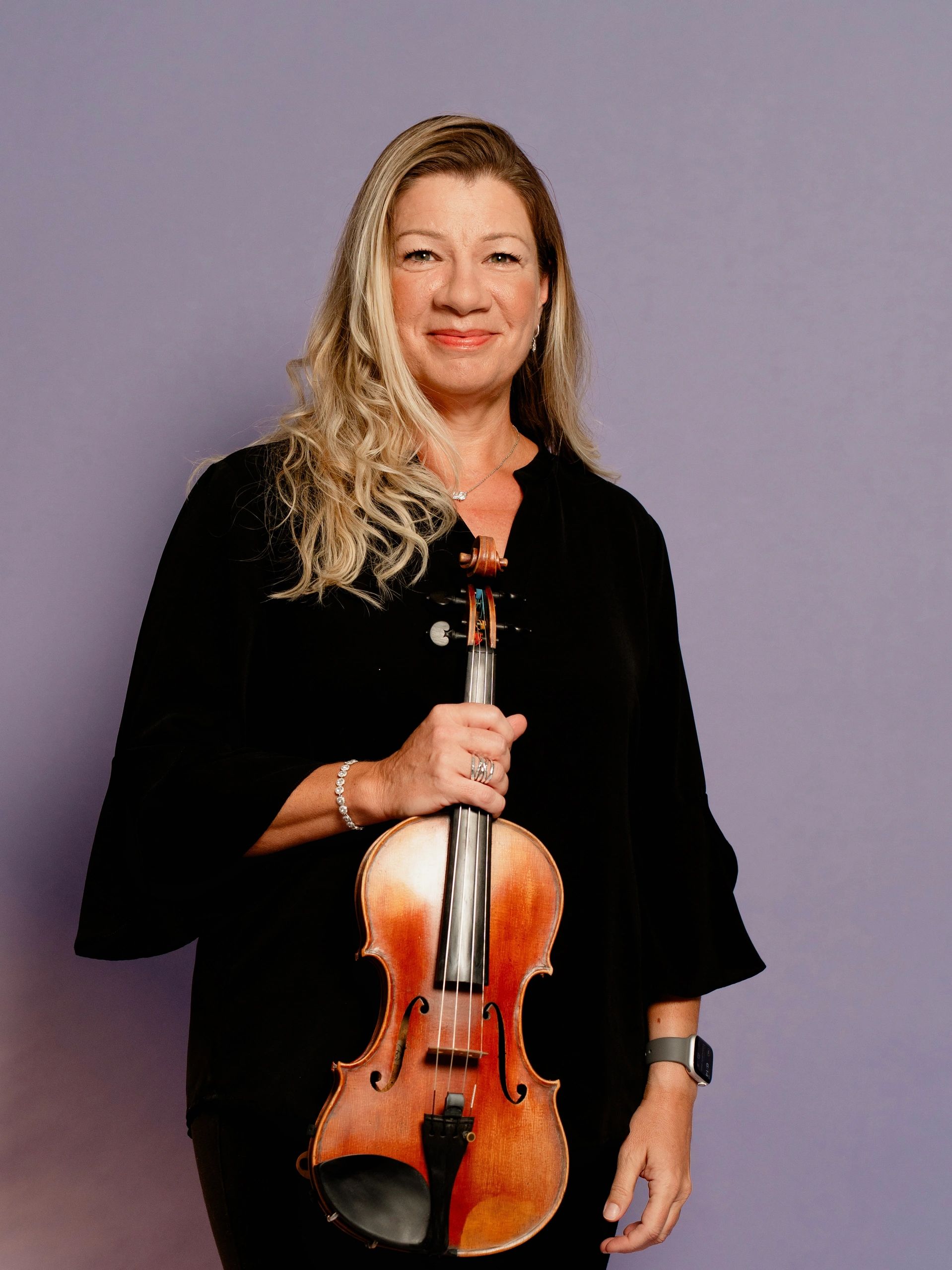 Smiling woman holding a violin against a purple background.