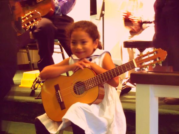A young girl happily holding a guitar during a musical event.