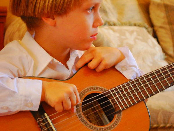 Young boy focused on playing an acoustic guitar indoors.