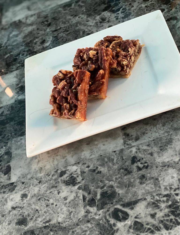 Three pecan bars on a white rectangular plate with a marble table background.