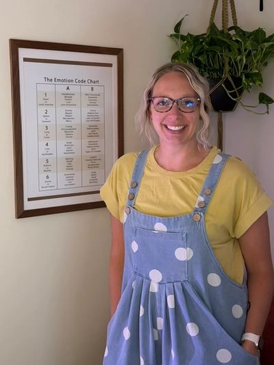 Smiling woman in glasses and polka dot dress stands by an emotion chart.