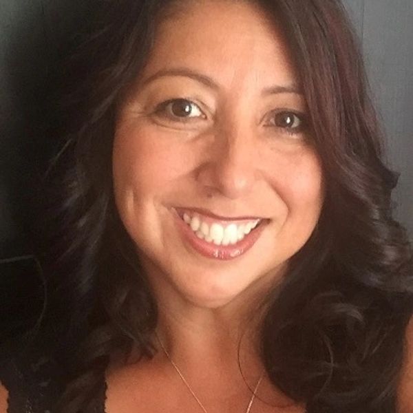 Smiling woman with dark wavy hair and warm brown eyes.