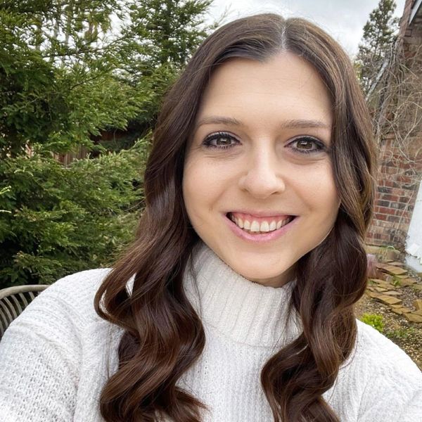 Smiling woman with long wavy hair in a white sweater outdoors.