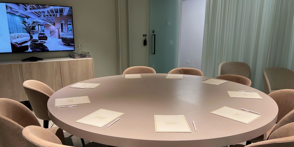 A large circular table with chairs surrounding the table. On the table there are papers with pens. 