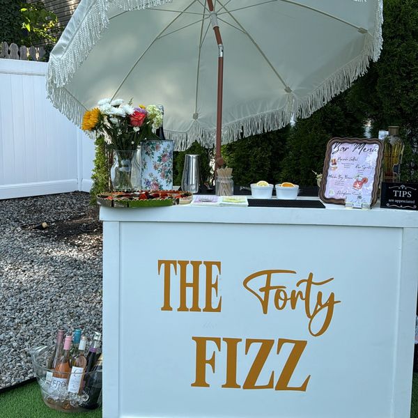 Outdoor drink stand with flowers and beverages under a white umbrella.