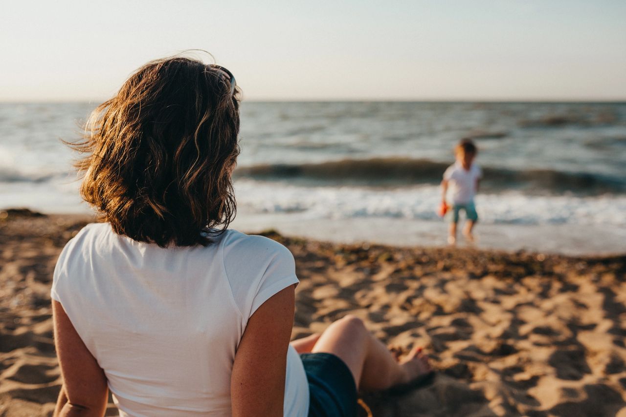 woman sitting on the beach watching her child play