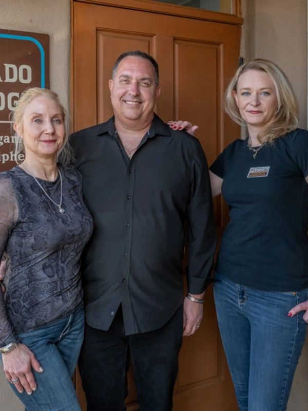 Three adults posing together in front of a door.