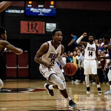 Basketball player dribbling during a game with teammates in the background.