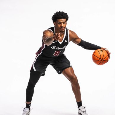 Basketball player in black uniform dribbling and pointing forward.