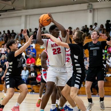 Basketball player in white holding the ball, guarded by three players in black uniforms.