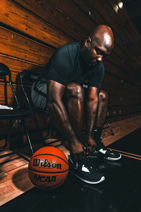 Athlete tying shoes next to a basketball on a gym floor.