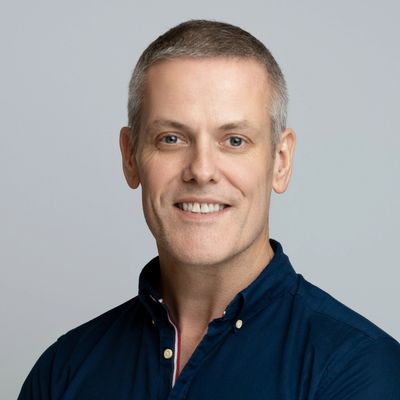 Smiling man in blue shirt against gray background.