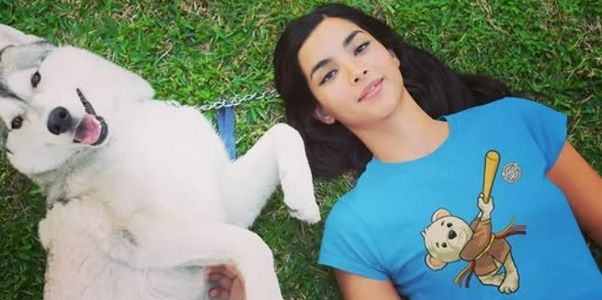 A woman lying on grass holding paws with a happy husky dog.