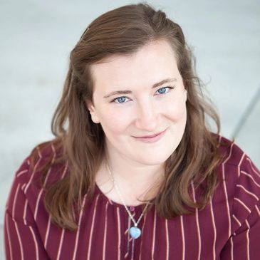 Smiling woman with blue eyes wearing a striped maroon top and heart-shaped necklace.