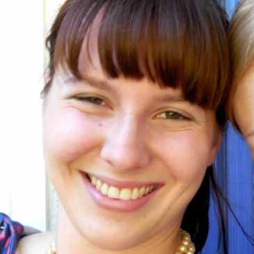 Smiling woman with bangs and a pearl necklace.
