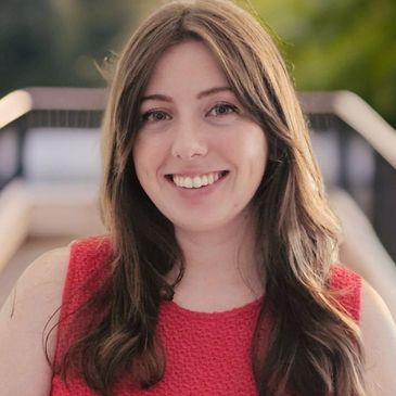 Smiling woman with long brown hair wearing a red sleeveless top.